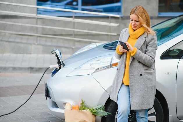 共享在一辆租来的电动车旁拿着电话的女人小型汽车持有系统