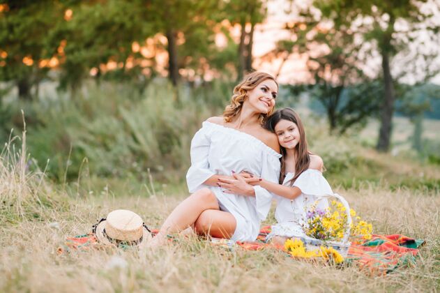 草地时尚的母亲和英俊的女儿享受大自然的乐趣花园团结休闲
