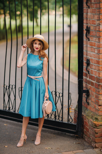 朋友街上穿着蓝色连衣裙戴着优雅帽子的时髦女孩化妆信心手提包