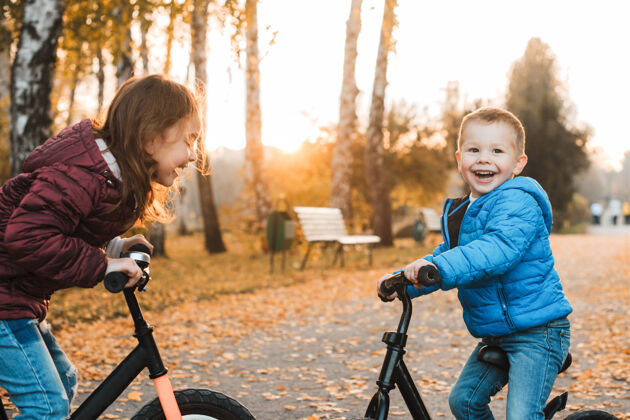 自行车可爱的小男孩在户外和妹妹面对面地坐在自行车上大笑户外公园活动