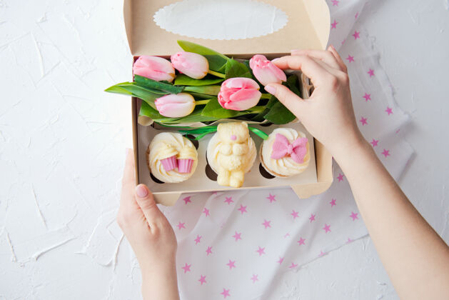 女士甜蜜的纸杯蛋糕和粉红色的花朵放在一个女人的手盒子里食品糖果甜点