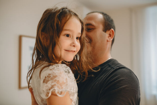 玩耍一张可爱女孩的特写照片 她在家里被父亲抱着微笑着看向别处年轻享受爱