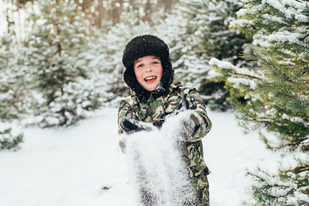人特写一张冬天森林里一个男孩的脸 他用雪吹手掌孩子雪轻皮肤