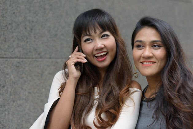 手机两位年轻的亚洲女商人在城市户外的合影城市朋友泰语