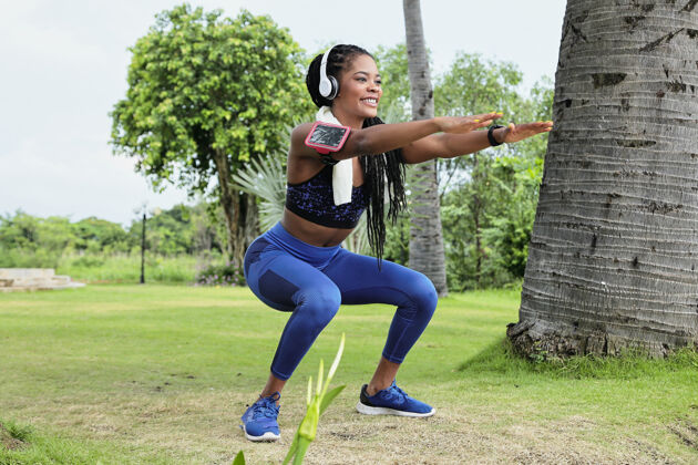 黑人快乐美丽的年轻黑人女运动员戴着耳机在公园里做蹲后晨练运动下蹲跑步