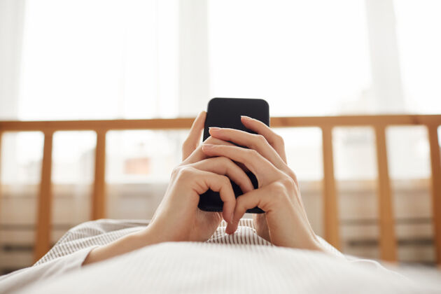 室内女人在床上休息时用手机输入信息的特写镜头舒适无线技术移动
