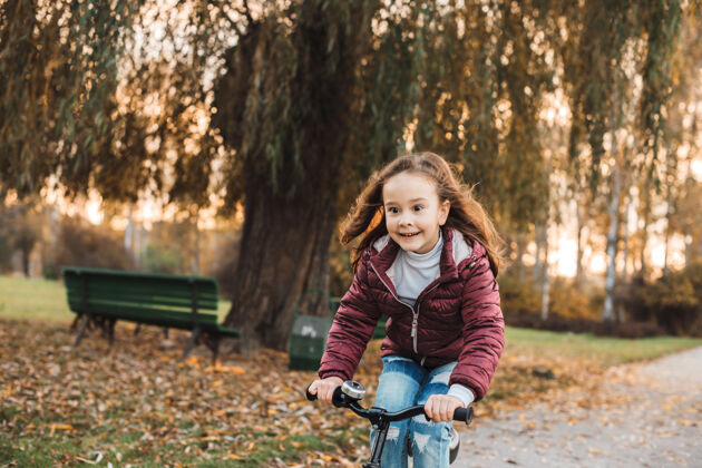 日落可爱的小女孩骑着自行车在公园里户外迎着夕阳表达自行车年轻