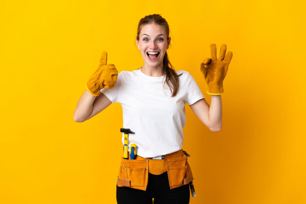 工人年轻的女电工隔离在黄色显示ok标志和拇指向上的手势工匠工艺手势