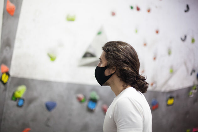 健身年轻健康的男性登山者戴着口罩在陡峭的岩石室内1攀岩努力