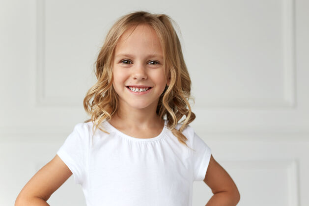 工作室正面肖像是一个小女孩微笑着看着镜头 穿着白衬衫 手放在她身上腰漂亮女孩金发快乐姿势