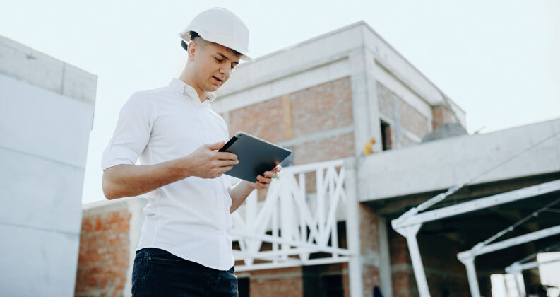 工业建筑工人戴着头盔 一边看平板电脑 一边制定未来的建筑规划工作服权力商业