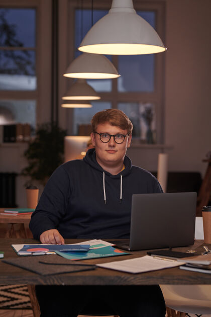 专业职业戴着眼镜的年轻商人的肖像 在办公室里拿着笔记本电脑在桌子旁工作 看着前面办公桌室内互联网
