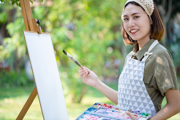绘画夏日田野里的亚洲美女 用画笔和彩色颜料在花园里的纸艺板上画画调色板自然美丽