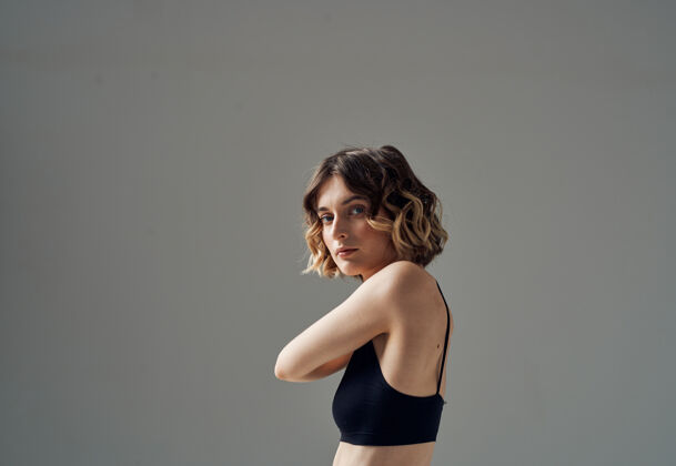 姿势一个穿着短T恤的女人站在灰色的墙上 用手在她裸露的肩膀上做瑜伽姿势健康人伸展