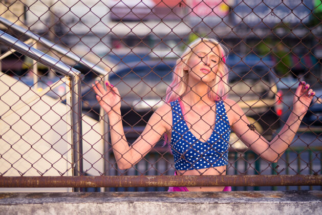 酷年轻漂亮的金发女人闭着眼睛 在户外拿着铁丝网围栏市中心人模特