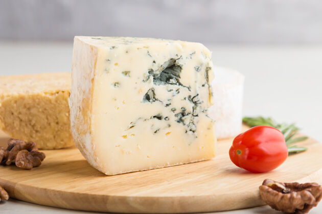 意大利蓝色奶酪和各种类型的奶酪 迷迭香和西红柿放在白色木板上不同组香料