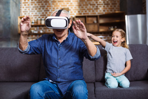 孩子快乐的老人微笑着测试虚拟现实设备 而他的孙女坐在附近科技现代一起