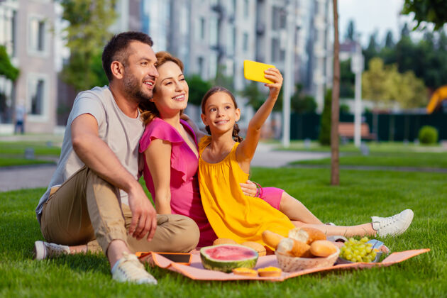 父亲家庭自拍快乐的漂亮女孩拿着她的智能手机和家人一起自拍友谊女儿野餐