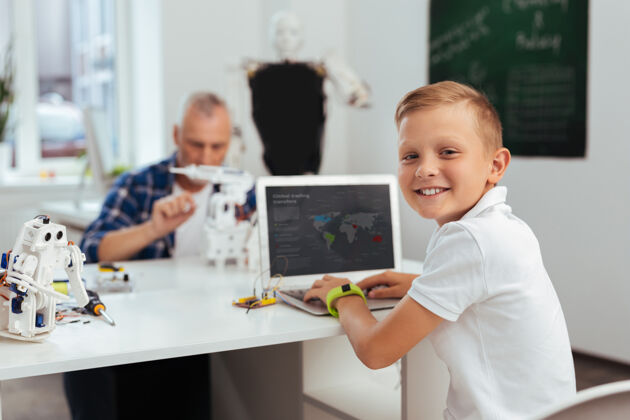 爱好积极的心情开朗快乐的男孩坐在电脑前对你微笑二进制社会保障干