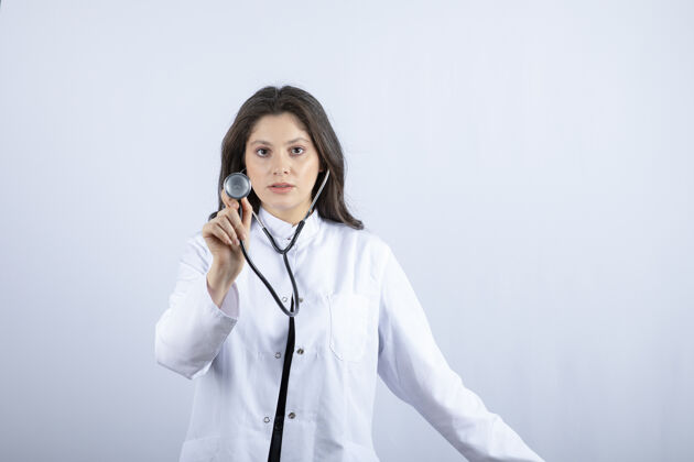 医药年轻女医生在白墙上用听诊器检查脉搏建议持有听诊器