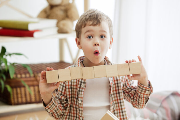 玩具坐在地板上的小孩在家里玩木块的男孩面带微笑 惊讶不已概念图 带复制品或负片空间 还有你的文本模型情感建设孩子