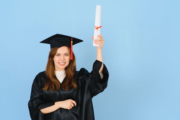 快乐戴着毕业帽和毕业礼服的女研究生 背景是蓝色的大学获奖者培训