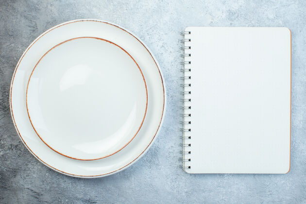 苦恼优雅的白色盘子和笔记本在灰色的表面与苦恼的表面与自由空间表面笔记本白色盘子