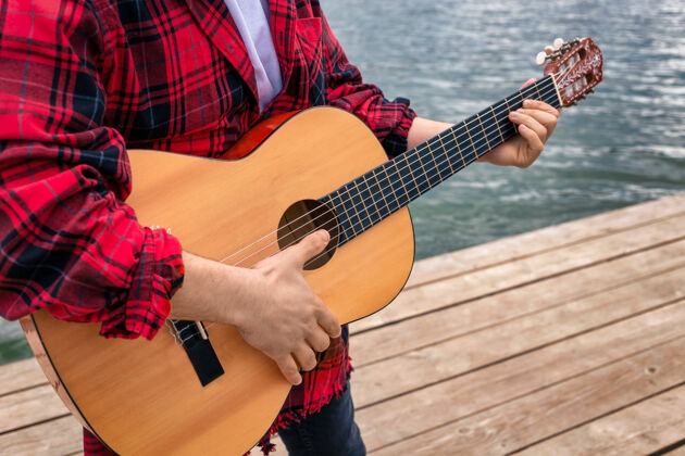 生活方式穿红衫的年轻人在公园的湖边弹吉他肖像热度男人