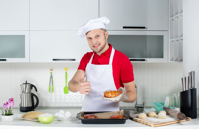 服务员在白色厨房里 年轻微笑的男厨师手持一个刚出炉的糕点 摆着ok的姿势男厨师视图支架