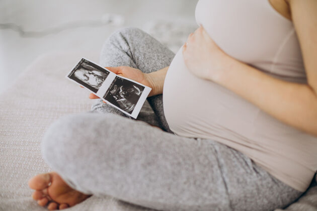 休闲孕妇带着超声波照片坐在床上生活产妇扫描