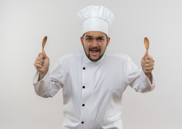 厨师愤怒的年轻男厨师穿着厨师制服 拿着勺子孤立在白墙上男制服愤怒