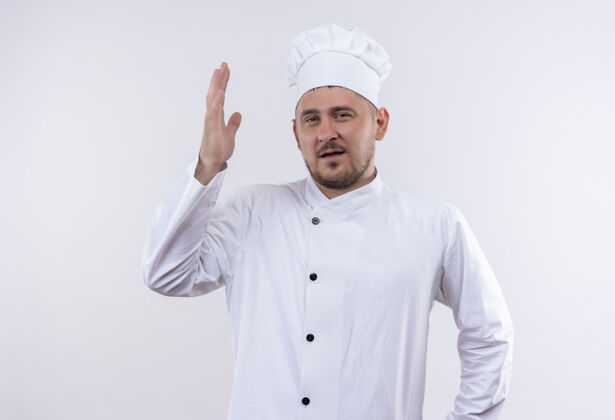 烹饪自信的年轻帅哥厨师身着厨师制服 举起的手孤立在白墙上年轻自信手