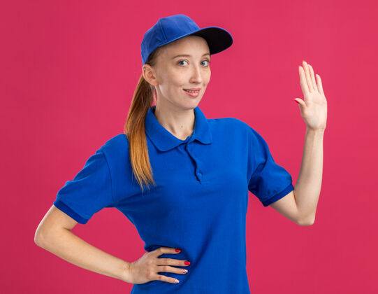 制服身穿蓝色制服 头戴鸭舌帽的年轻送货女孩微笑着自信地张开双臂站在粉色的墙上微笑女孩帽子