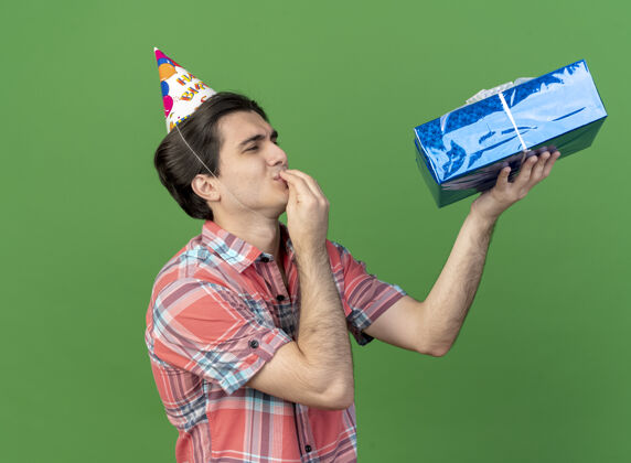 站着兴奋的白种人帅哥戴着生日帽站在一边拿着礼物盒看着美味的标志美味空间拿着