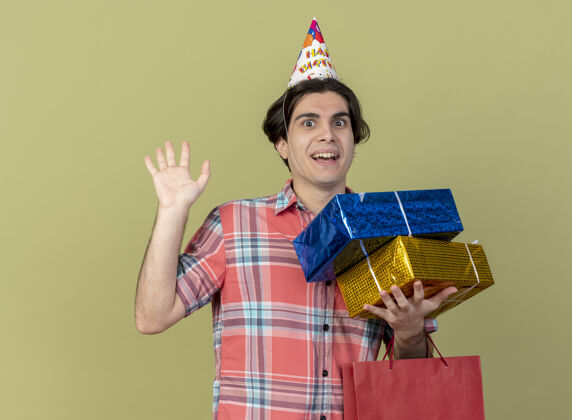 生日一个戴着生日帽 手举礼品盒和纸质购物袋的帅哥站在那里 惊讶不已举行站礼物