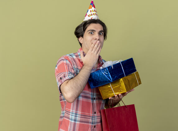 包帅气的白种人戴着生日帽手持礼品盒和纸购物袋盒子橄榄生日