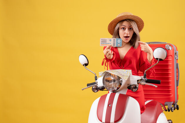 人坐在轻便摩托车上的年轻女士拿着红色的手提箱 手里拿着票时尚成人模型