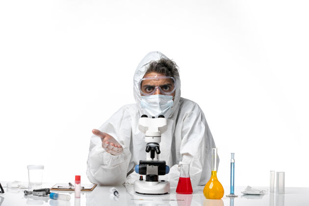 面罩穿防护服戴口罩的男医生用显微镜对着白色防护罩子视图防护服