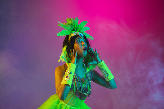 戏剧美丽的年轻女子在狂欢节 时尚的化装舞会服装与羽毛跳舞的梯度墙上霓虹灯美丽时尚庆典