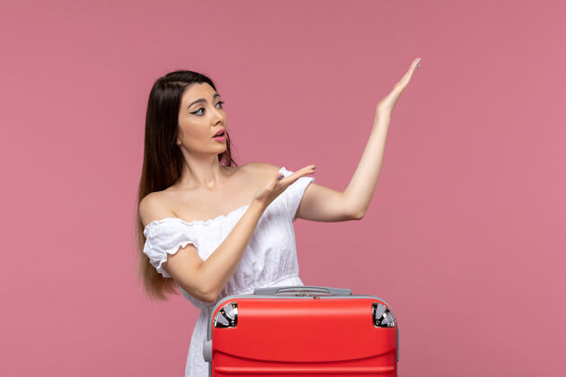 年轻女性正面图：年轻女性带着红色书包在粉色书桌上准备度假出国旅行海上旅行包准备旅行