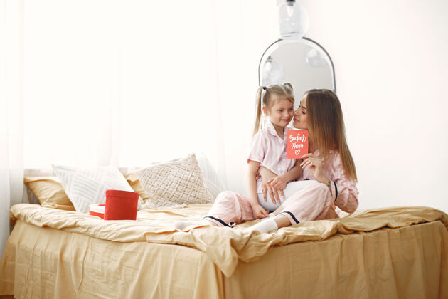 家庭母女倆在床上享受著手里拿著紅色的禮盒母親節室內慶典愛