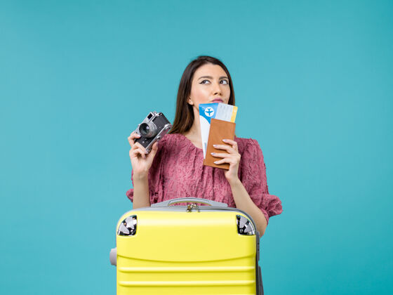 相机前景年轻女子拿着相机和机票去度假淡蓝色背景旅行度假女子出海微笑美女旅程