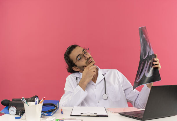 医学年轻的男医生戴着医用眼镜 穿着医用长袍 听诊器坐在办公桌旁思考眼镜男性