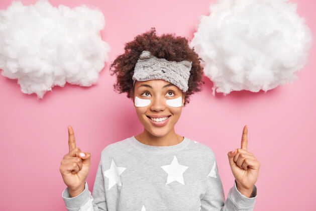 卷发积极的年轻卷发女士戴着睡眠面罩和睡衣在眼睛下面贴上美容贴片点在白云上面广告睡眠产品有好心情秀休闲醒来