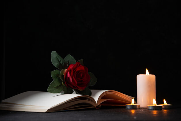 死亡在黑暗的表面上燃烧着打开的书和红花蜡烛的正面视图花瓣红黑暗