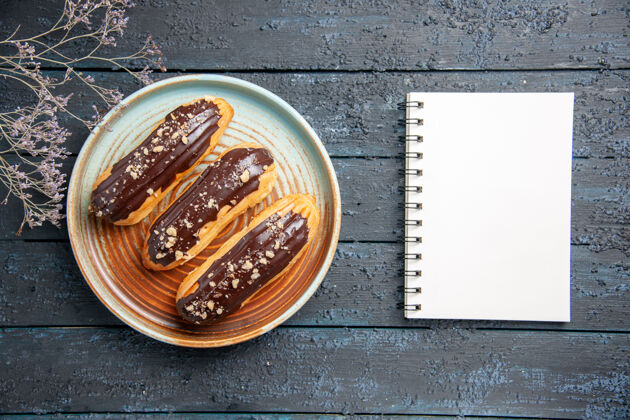 咖啡俯视图：椭圆形平板上的巧克力色干花枝和深色木桌上的笔记本饭美食干