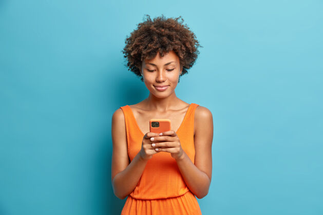 科技满意的年轻女子的肖像在智能手机上查看新闻 穿着露肩的裙子 使用高速互联网 永远保持联系 隔着蓝色的墙自然阅读检查