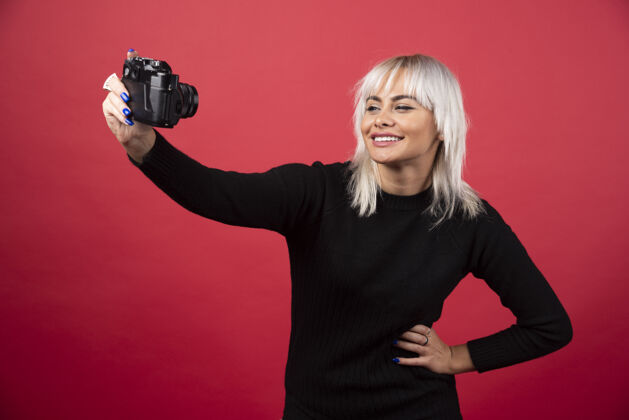 摄影师年轻女子用红色背景的照相机拍照高质量的照片女性化年轻人手