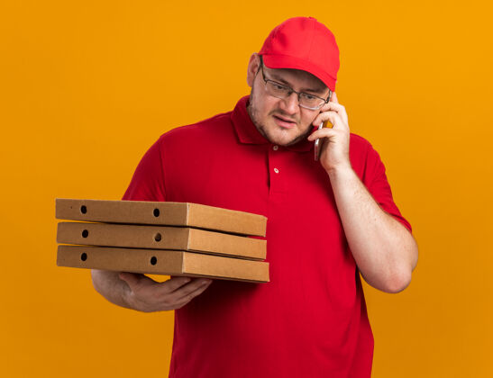 孤立自信超重的年轻送货员 戴着眼镜 拿着比萨饼盒 在橘黄色的墙上 隔着复印空间 讲着电话眼镜信心电话