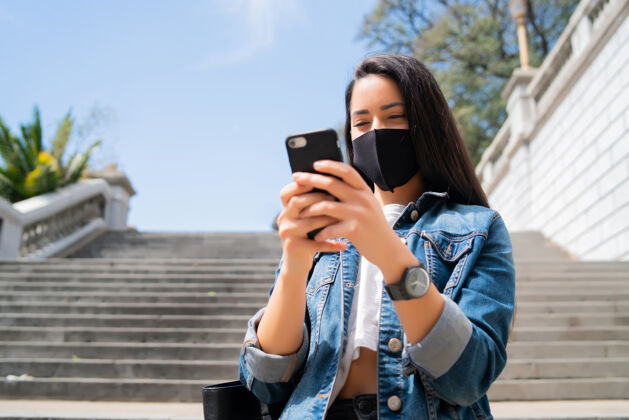 面罩年轻女子戴着防护面具 站在街上使用手机的画像手机电话手机